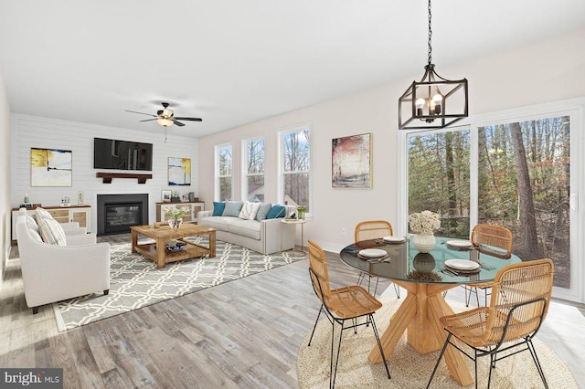 interior space with a glass covered fireplace, baseboards, light wood finished floors, and ceiling fan with notable chandelier