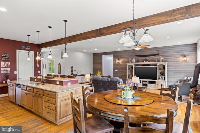 dining space featuring sink, light wood-type flooring, wooden walls, ceiling fan, and beam ceiling