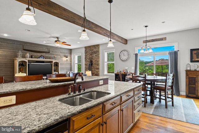 kitchen featuring sink, light wood-type flooring, pendant lighting, beam ceiling, and light stone countertops