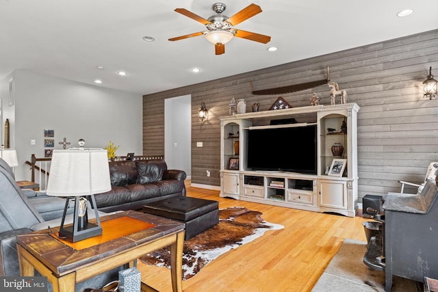 living room featuring ceiling fan, wooden walls, and light wood-type flooring