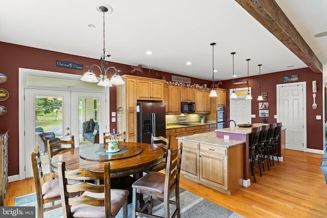 kitchen with light stone counters, black appliances, an island with sink, decorative light fixtures, and light wood-type flooring