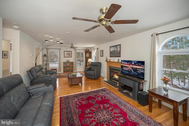 living area with light wood finished floors, a fireplace with flush hearth, and a ceiling fan