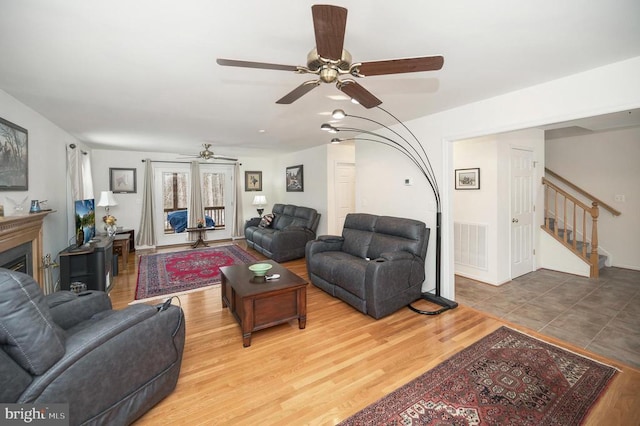 living room with wood finished floors, visible vents, a fireplace, ceiling fan, and stairs