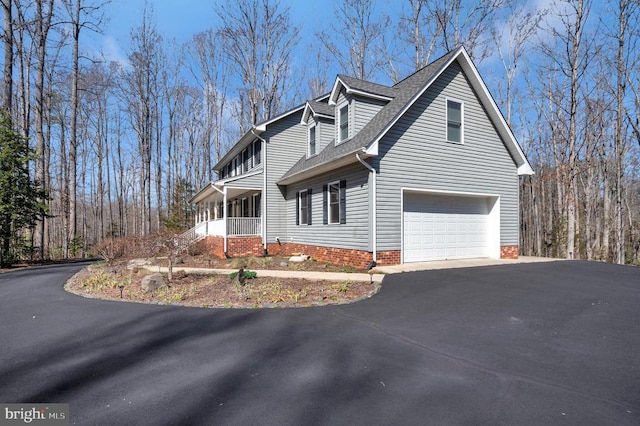 view of side of property featuring a garage, a porch, driveway, and a shingled roof
