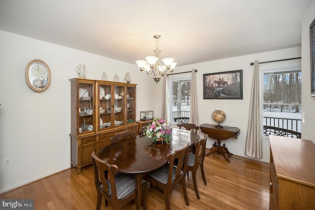 dining room with light wood-style flooring, a notable chandelier, a healthy amount of sunlight, and baseboards