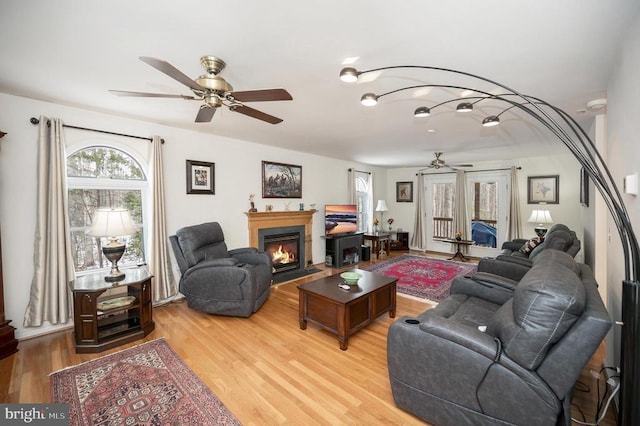 living room featuring a ceiling fan, light wood-type flooring, and a lit fireplace