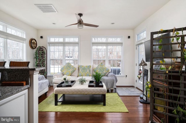 living area with visible vents, baseboards, dark wood-type flooring, and a ceiling fan