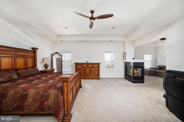 bedroom featuring a ceiling fan, light colored carpet, and a multi sided fireplace