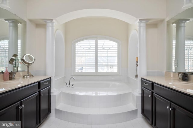 bathroom featuring two vanities, decorative columns, a bath, and a sink