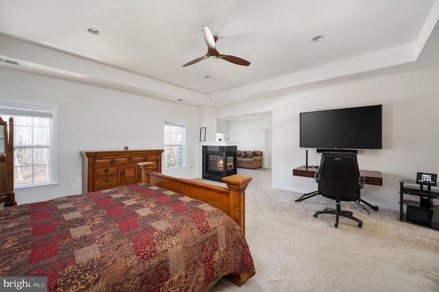 carpeted bedroom featuring a tray ceiling, a multi sided fireplace, baseboards, and visible vents