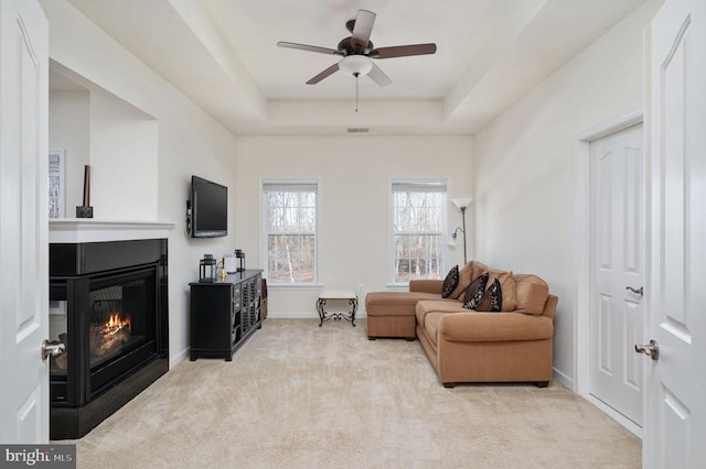 carpeted living area with visible vents, ceiling fan, baseboards, a multi sided fireplace, and a raised ceiling