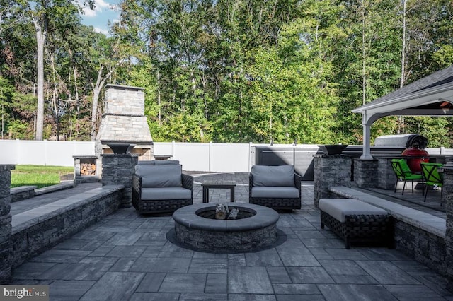 view of patio featuring a view of trees, an outdoor stone fireplace, and fence