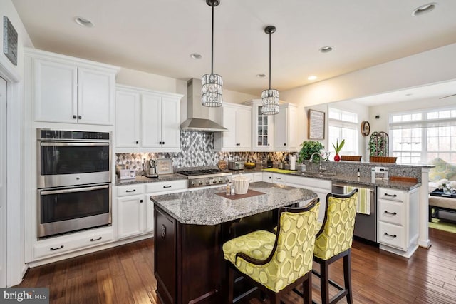 kitchen with stainless steel appliances, a peninsula, a breakfast bar area, wall chimney range hood, and decorative backsplash