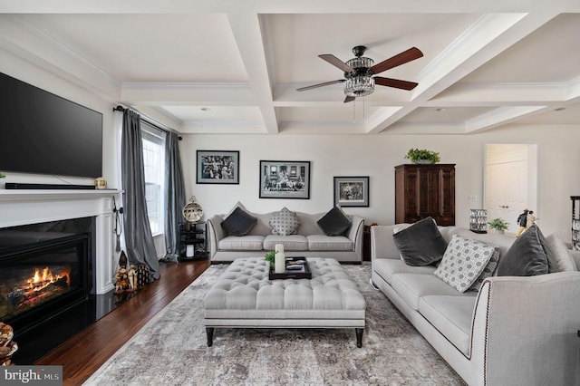 living room with beam ceiling, a ceiling fan, coffered ceiling, a glass covered fireplace, and wood finished floors