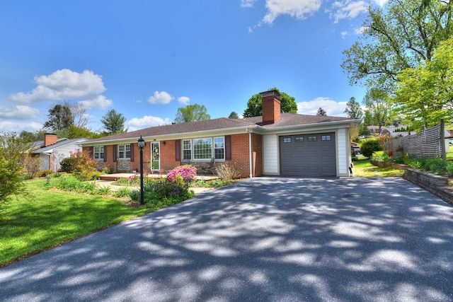 single story home featuring a garage, a front lawn, a chimney, brick siding, and driveway