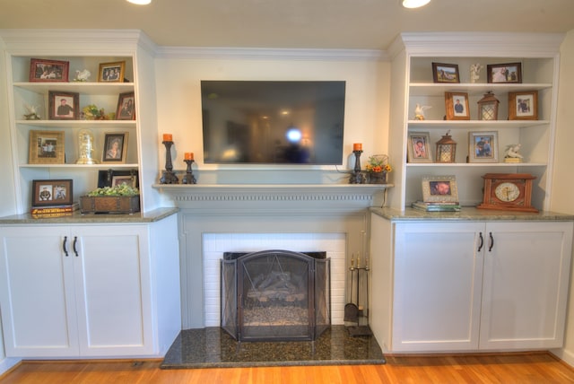 living area with crown molding, a fireplace with raised hearth, and light wood finished floors