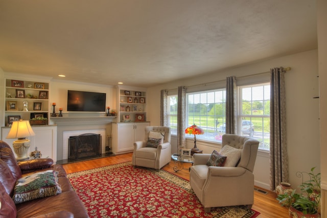 living room featuring a fireplace, light wood finished floors, built in shelves, and visible vents
