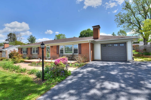single story home with an attached garage, a chimney, brick siding, and aphalt driveway