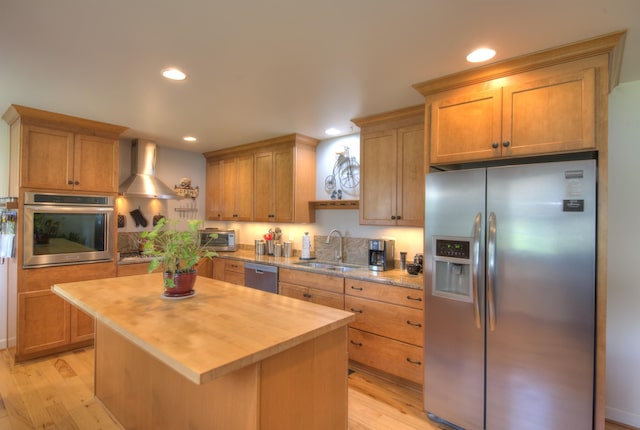 kitchen featuring butcher block countertops, wall chimney exhaust hood, a sink, light wood finished floors, and appliances with stainless steel finishes