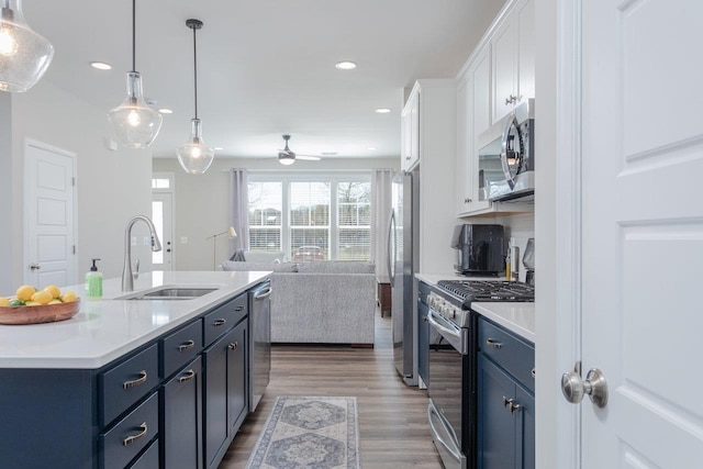 kitchen with a sink, open floor plan, white cabinetry, light countertops, and appliances with stainless steel finishes