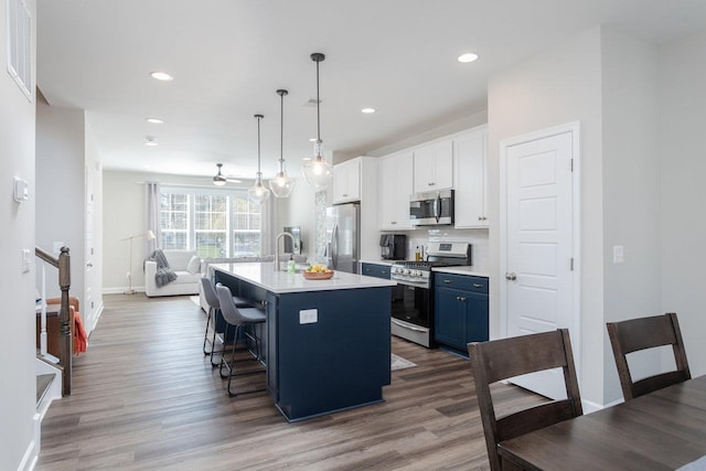 kitchen featuring stainless steel appliances, a kitchen breakfast bar, wood finished floors, and an island with sink