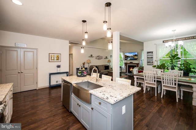 kitchen with stainless steel dishwasher, light stone countertops, a sink, a warm lit fireplace, and dark wood-type flooring