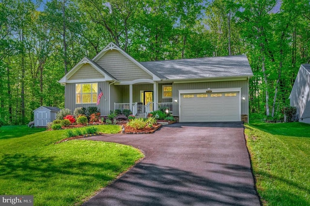 view of front of property featuring a garage, covered porch, driveway, a front yard, and a storage shed