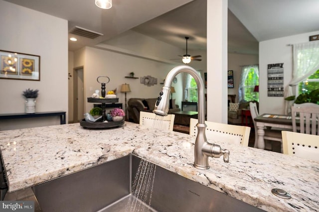 kitchen with visible vents, a ceiling fan, light stone counters, and open floor plan