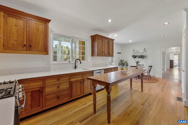 kitchen featuring brown cabinetry, stainless steel appliances, a sink, light countertops, and light wood-style floors