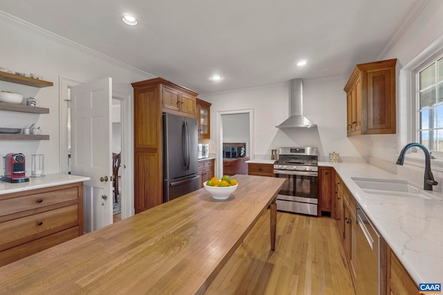 kitchen featuring crown molding, wall chimney range hood, brown cabinetry, stainless steel appliances, and a sink