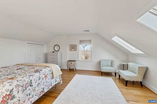 bedroom with visible vents, lofted ceiling with skylight, baseboards, and light wood finished floors