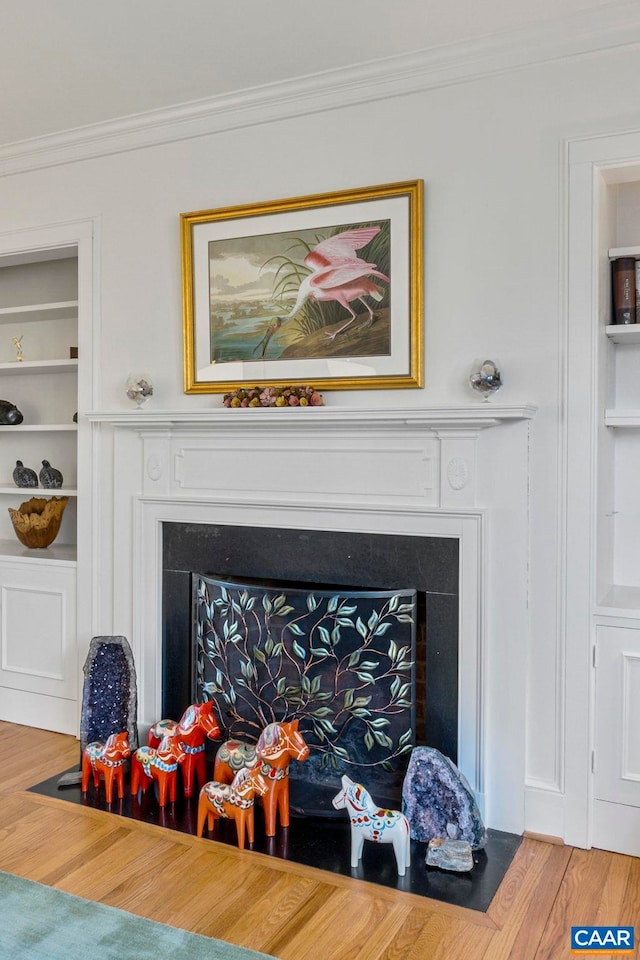 room details featuring crown molding, wood finished floors, a fireplace, and built in features