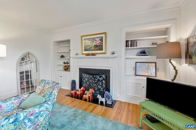 living area with light wood-style flooring, a fireplace with flush hearth, built in shelves, and ornamental molding