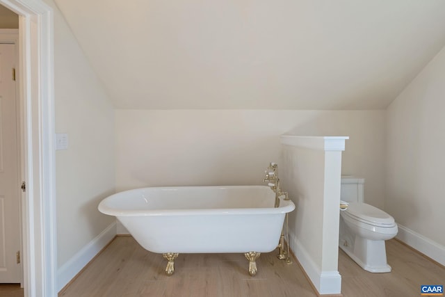 bathroom featuring baseboards, toilet, lofted ceiling, wood finished floors, and a soaking tub