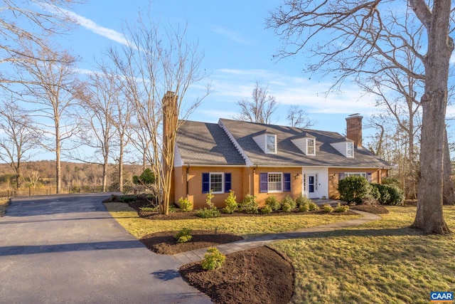 cape cod-style house featuring brick siding, a chimney, and a front lawn