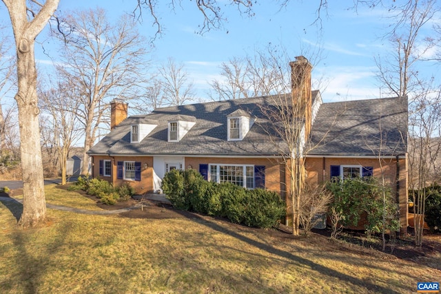 cape cod-style house featuring brick siding, a chimney, a front lawn, and roof with shingles