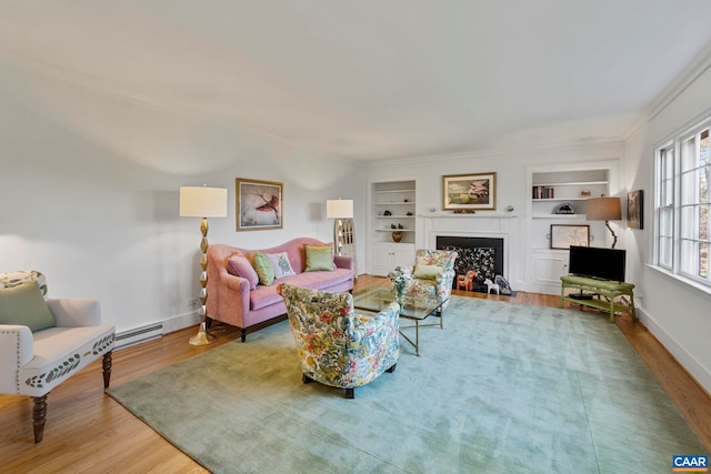 living room featuring built in shelves, a fireplace with flush hearth, ornamental molding, wood finished floors, and baseboards