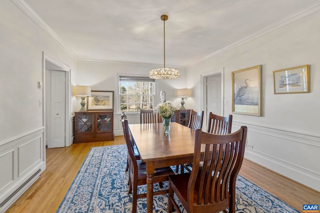 dining space with light wood finished floors, a wainscoted wall, and crown molding