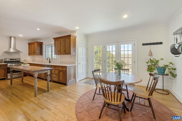 kitchen featuring brown cabinetry, light wood finished floors, appliances with stainless steel finishes, and wall chimney range hood