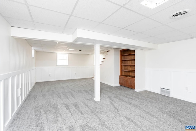 basement featuring a drop ceiling, built in features, and light colored carpet