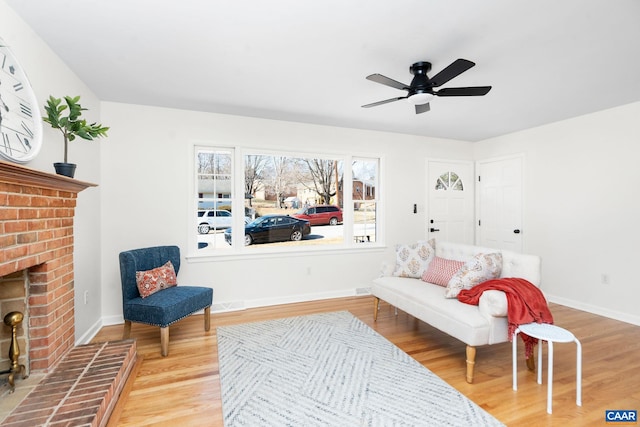 sitting room with a brick fireplace, hardwood / wood-style floors, and ceiling fan