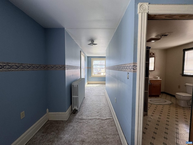 hallway with baseboards, radiator, and carpet floors