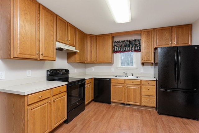 kitchen featuring light wood-style flooring, under cabinet range hood, a sink, light countertops, and black appliances