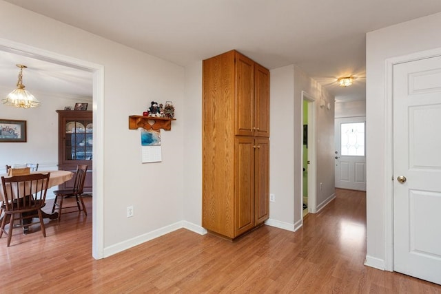 hallway with light wood finished floors, baseboards, and a notable chandelier