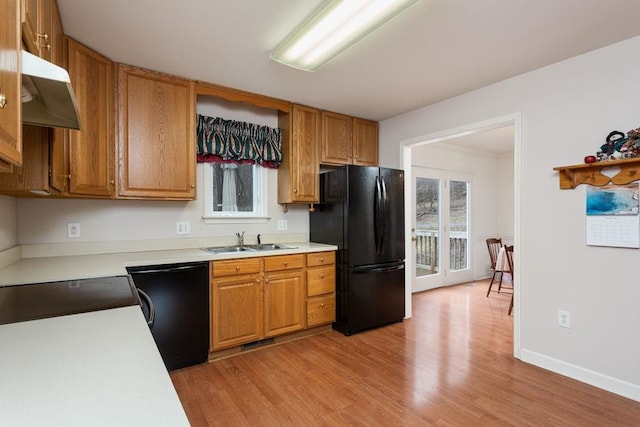 kitchen with under cabinet range hood, a sink, light wood-style floors, light countertops, and black appliances