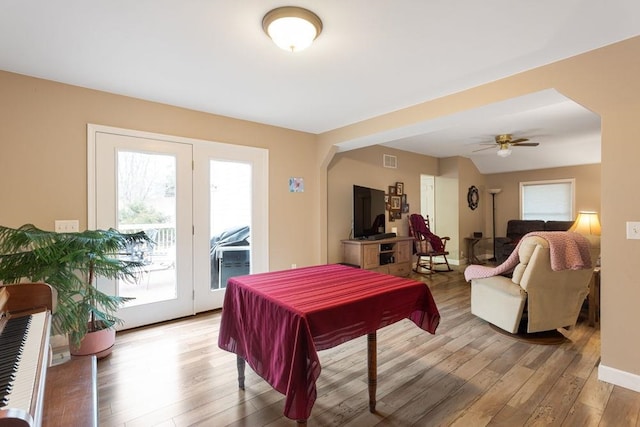 dining space with arched walkways, light wood-style flooring, a ceiling fan, visible vents, and baseboards