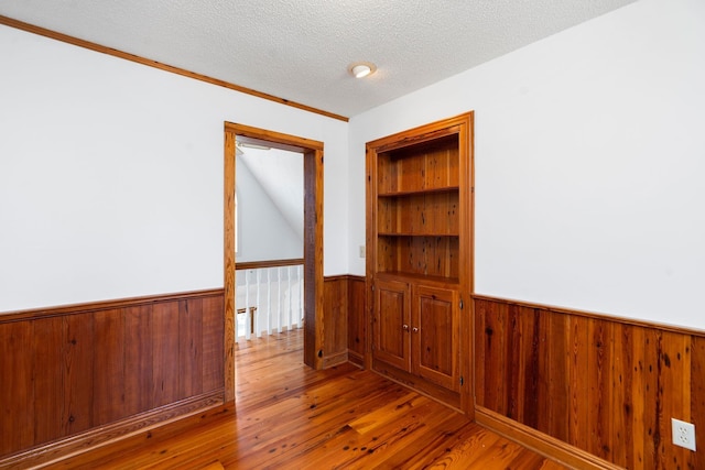 unfurnished room featuring hardwood / wood-style flooring, built in features, a textured ceiling, and wooden walls