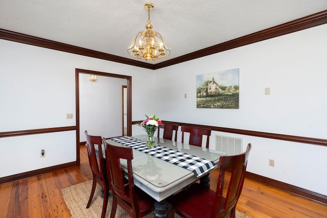 dining room with a textured ceiling, hardwood / wood-style floors, crown molding, and a chandelier