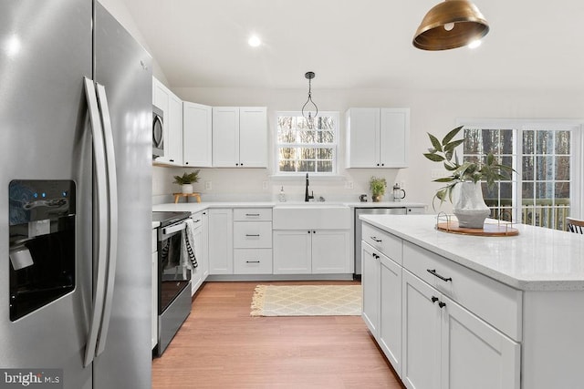 kitchen featuring sink, appliances with stainless steel finishes, white cabinets, decorative light fixtures, and light wood-type flooring