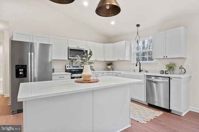 kitchen with a kitchen island, white cabinets, hanging light fixtures, stainless steel appliances, and light wood-type flooring